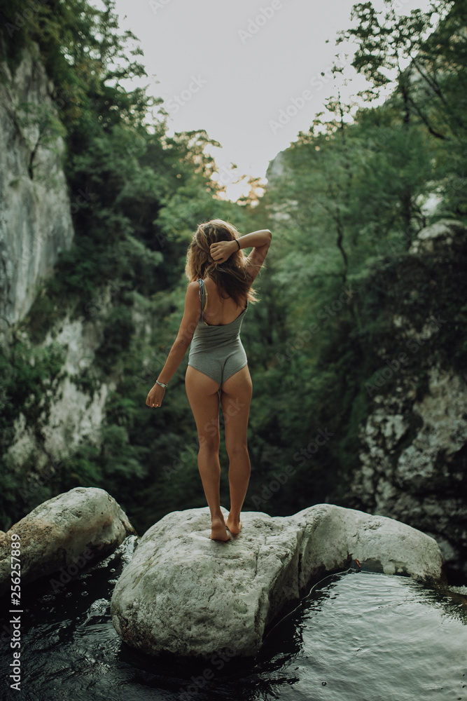 Young and sexy woman stand on rock wearing swimsuit on the beautiful waterfall in the jungle beside cliff Young and sexy woman stand on rock wearing swimsuit on the beautiful waterfall in the jungle beside cliff