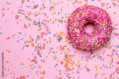 Sweet pink donut with multicolored sprinkles on a pink background flat lay