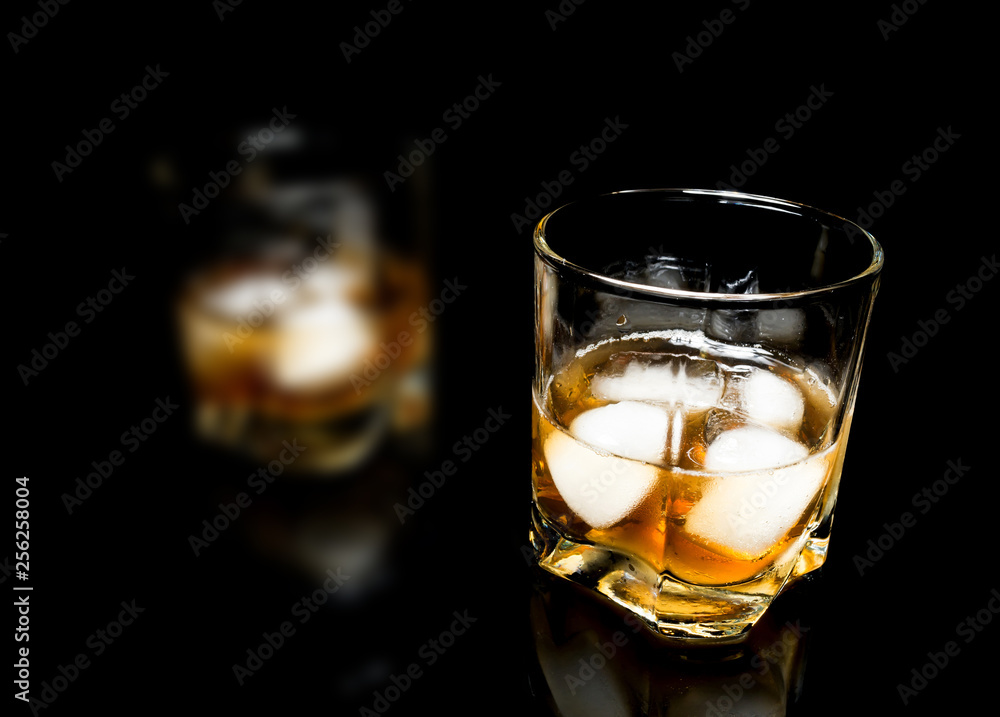 Whiskey with ice close up on a glass table isolated on a black background