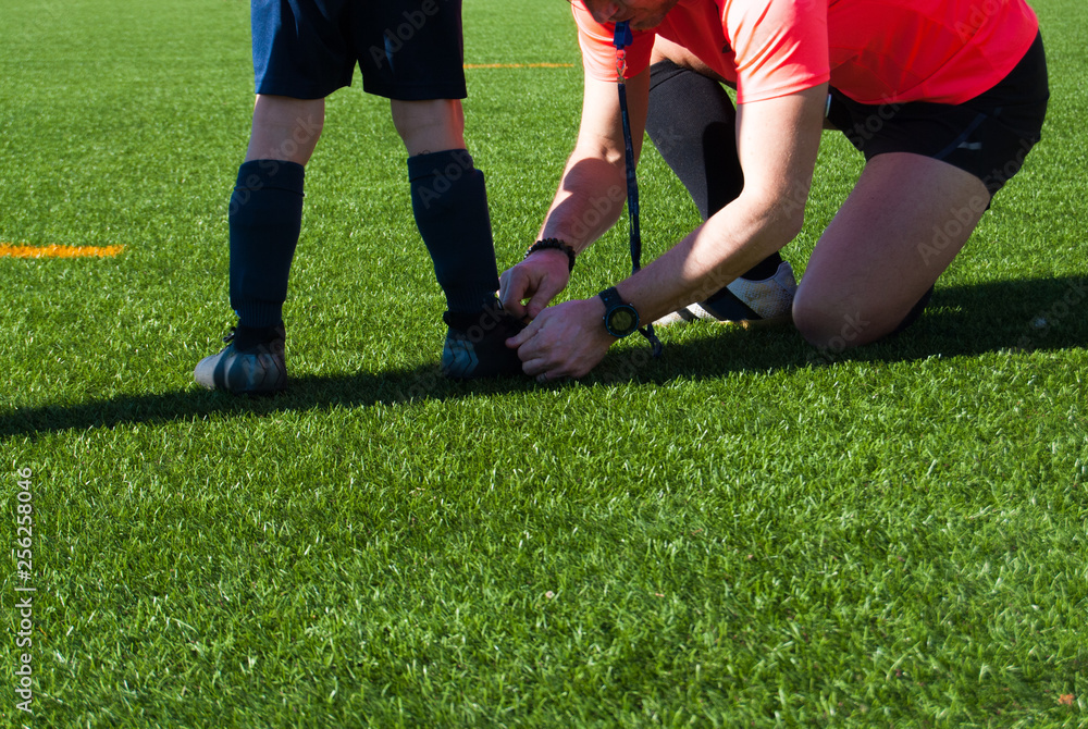 Fototapeta premium Referee tying a shoe to a child soccer player
