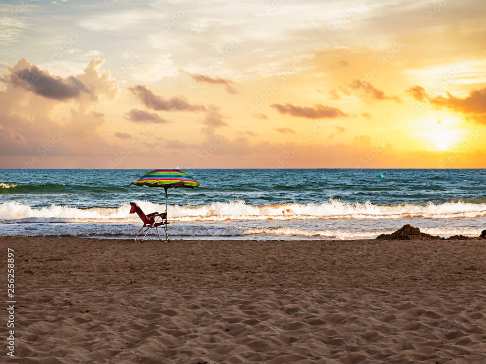 striped umbrella and chair at the first beach line at sunset striped umbrella and chair at the first beach line at sunset