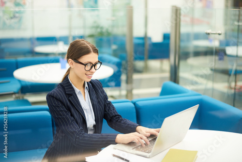 Portrait of young businesswoman wearing glasses using laptop in office during internship in corporate enterprise, copy space