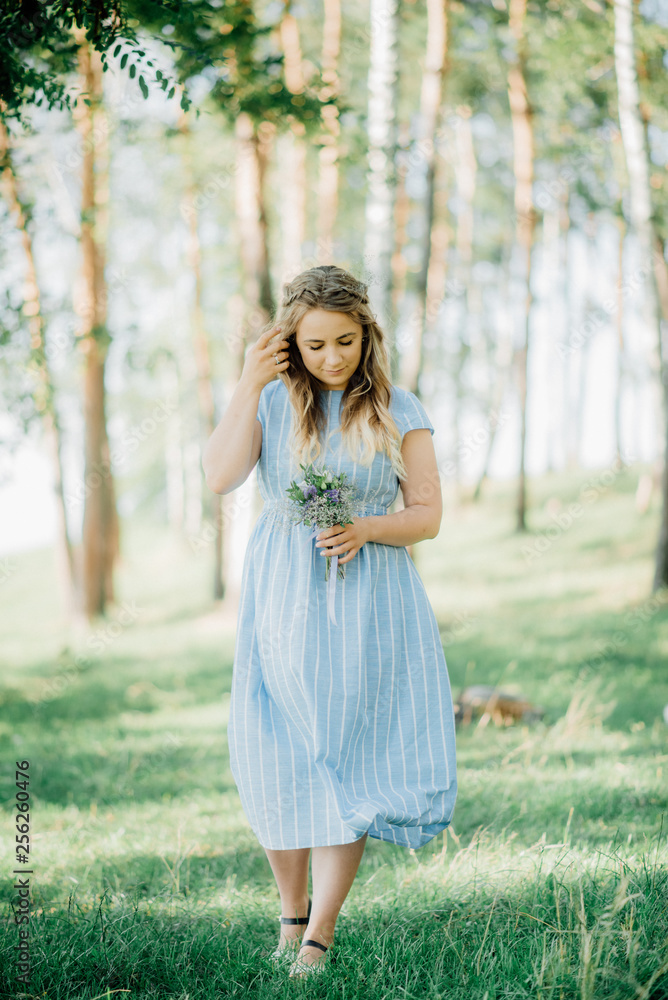 A beautiful blond female in a blue dress walks in a park in a sunny weather. A pretty girl smiles. A beautiful blond female in a blue dress walks in a park in a sunny weather. A pretty girl smiles.