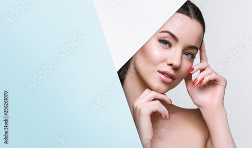 Portrait of young beautiful woman with healthy glow perfect smooth skin look into the hole of colored paper. Model with natural nude make up peers into hole in pink paper. Fashion, beauty, skincare. © KDdesignphoto