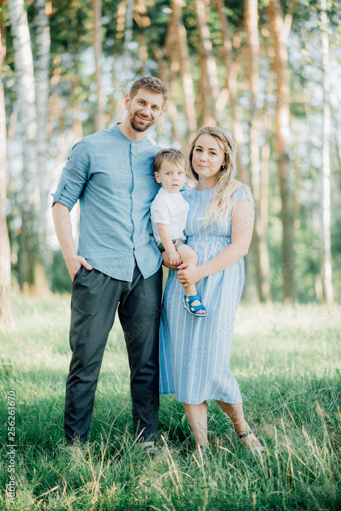mother holding her son at a photo shoot to help him right pose for the photographer. Happy young family  outside in green nature