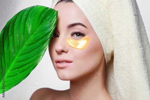 Portrait of young beautiful woman with healthy glow perfect smooth skin holds green tropical leaf. Gold cosmetics collagen hydrogel patch. Lifting anti-wrinkle mask under eyes. Skincare concept. photo