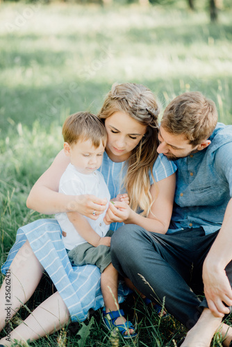 happy parents hugging their son lying on a green grass in the woods. The concept of a happy young family. Parents smile with the child. Ideal family