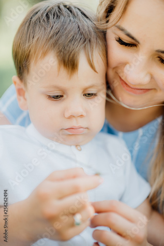 mother holding her son at a photo shoot to help him right pose for the photographer. Happy young family outside in green nature