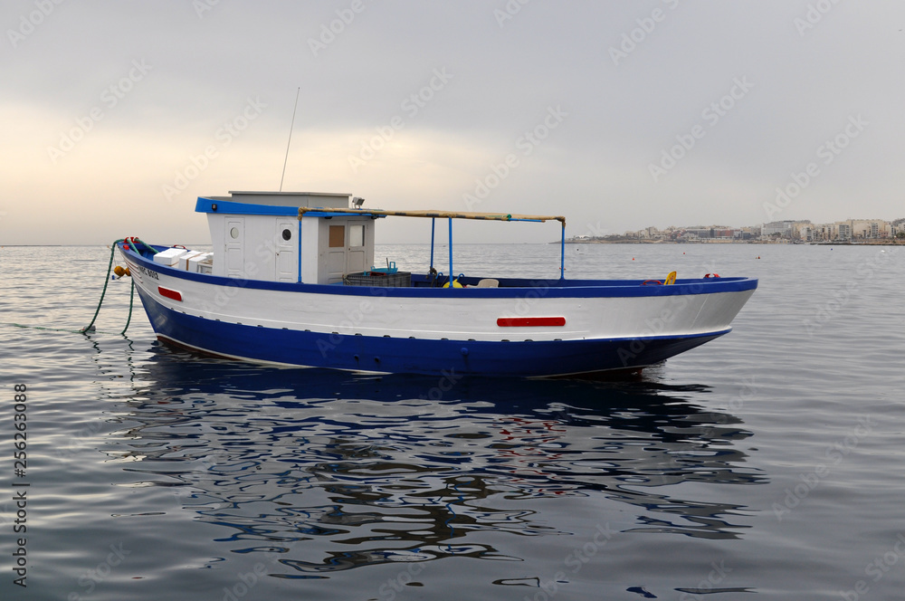 A lonely boat in the sea at sunset painted in blue and white A lonely boat in the sea at sunset painted in blue and white