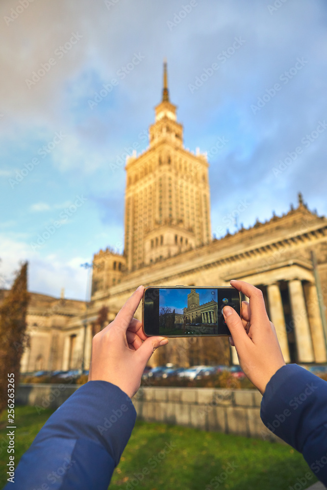 Obraz premium Young female tourist walking around the city and making photo near Palace of Culture and Science in Warsaw. Having a happy vacation in Poland