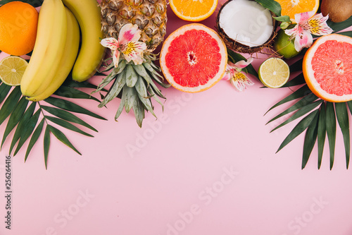 Summer fruits. Tropical palm leaves, pineapple, coconut, grapefruit, orange and bananas on pink background. Flat lay, top view, copy space