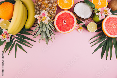 Summer fruits. Tropical palm leaves, pineapple, coconut, grapefruit, orange and bananas on pink background. Flat lay, top view, copy space photo