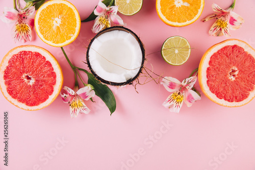 Summer tropical fruits. Coconut, grapefruit, orange and lime around alstroemeria flower on pink background. Flat lay, top view, copy space