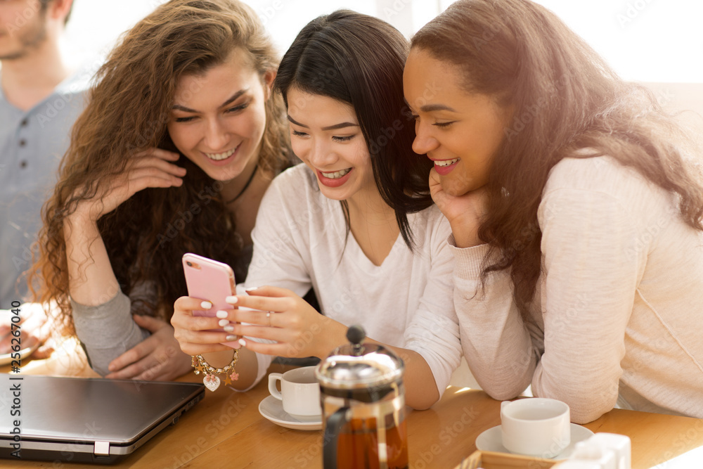 Young cheerful friends using smart phone together at the coffee shop Young cheerful friends using smart phone together at the coffee shop