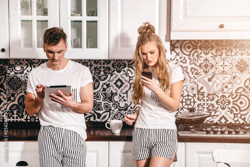 Internet addicted couple standing at tge kitchen with the gadgets photo