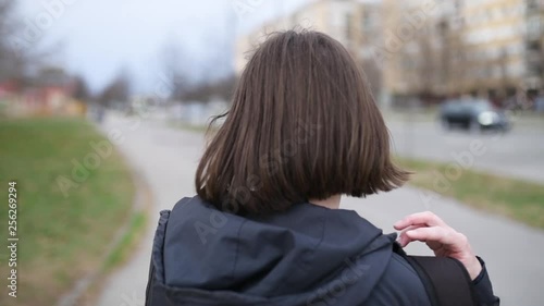 Rear view of woman pulling down backpack on street, slow motion handheld footage