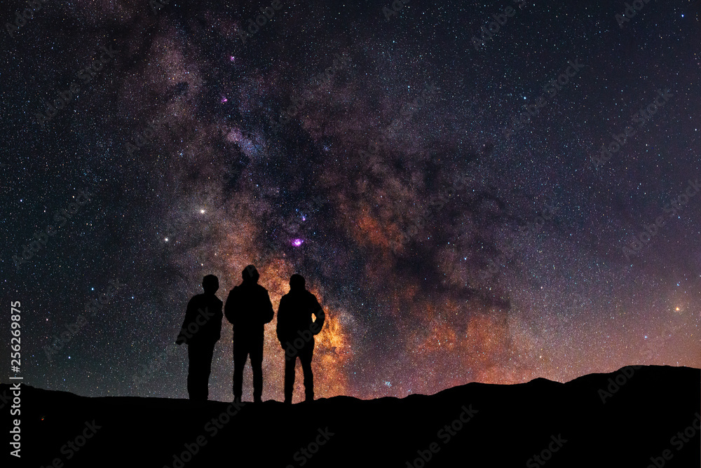 Three silhouettes stand on a hill and look at the close up milky way galaxy.