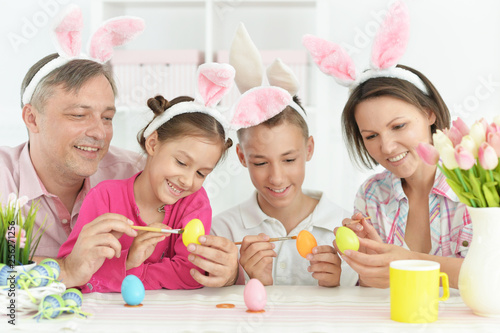 Portrait of happy family of four wearing bunny ears and painting Easter eggs at home