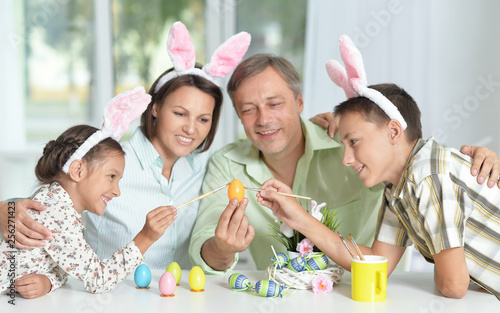 Happy family of four wearing bunny ears and painting Easter eggs 