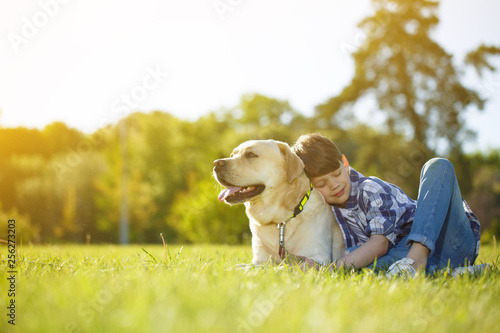 Young cheerful boy resting at the park with his dog
