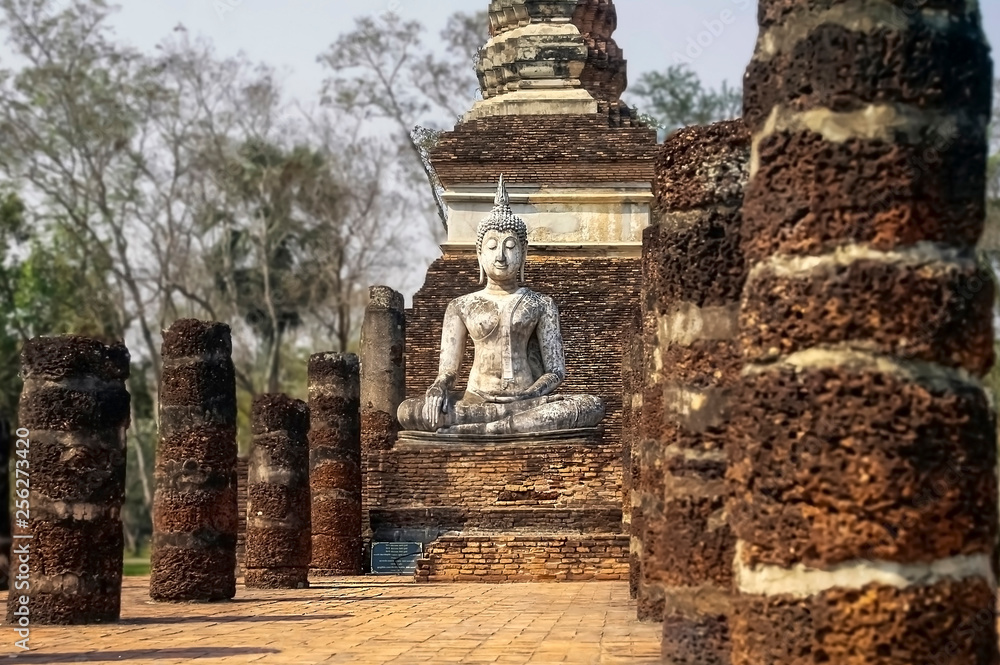 Ancient statue of a meditating Buddha among columns in Sukhothai National Park, Thailand