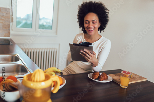 Smiling young African female using digital tablet in kitchen