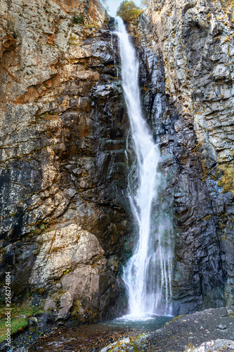 Bright colorful  very high mountain waterfall with mineral iron water falling from the rock.