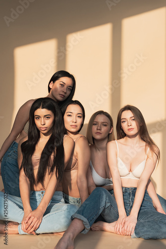 five pensive multicultural girls sitting in sunlight and looking at camera