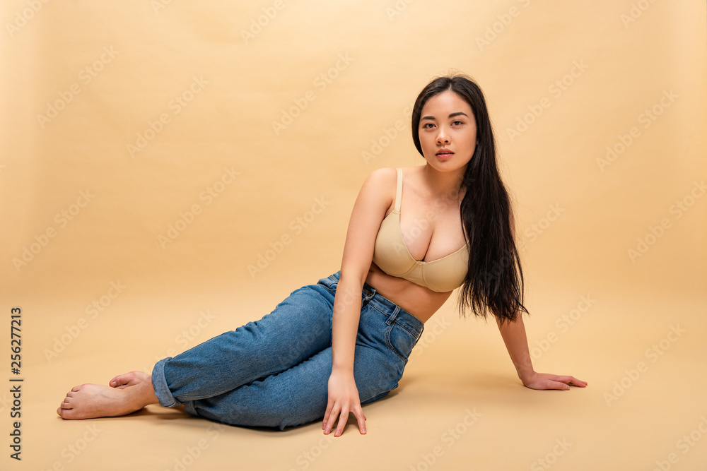pretty girl in blue jeans and bra sitting and looking at camera, body positivity concept pretty girl in blue jeans and bra sitting and looking at camera, body positivity concept