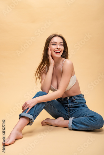 happy pretty girl in blue jeans and bra sitting and holding hand near face