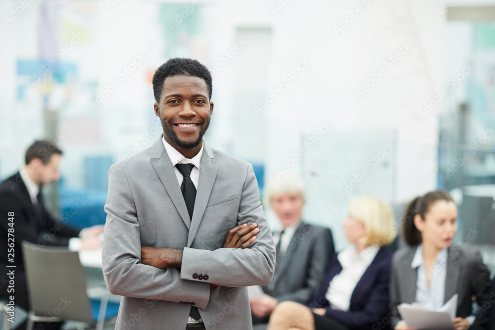 Waist up portrait of successful African-American businessman smiling at camera while posing in office standing with arms crossed, copy space Waist up portrait of successful African-American businessman smiling at camera while posing in office standing with arms crossed, copy space