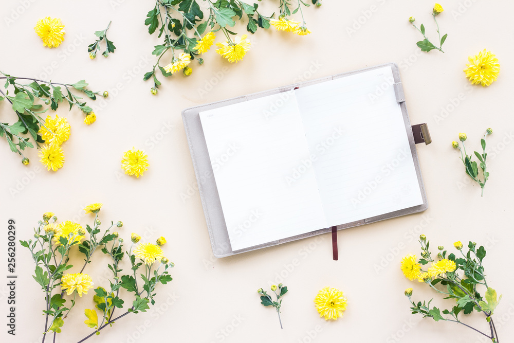 Fotografie Yellow flowers, notebook on beige background, flat lay, top view