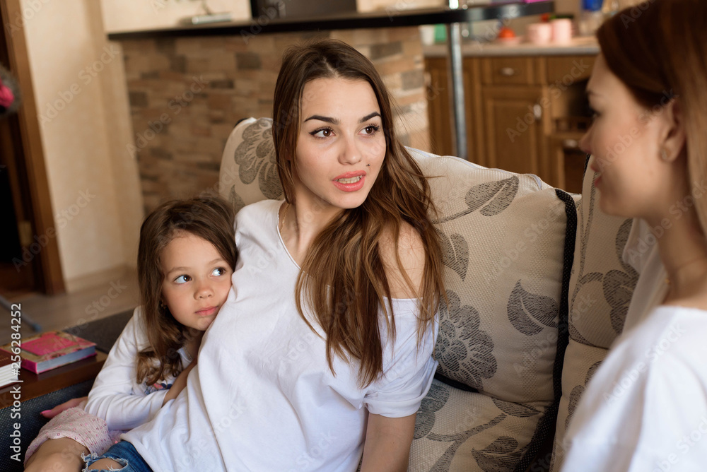 Portrait of two sisters and a little girl sitting on the couch, smiling. Concept: family, sisters, home and happiness. Portrait of two sisters and a little girl sitting on the couch, smiling. Concept: family, sisters, home and happiness.