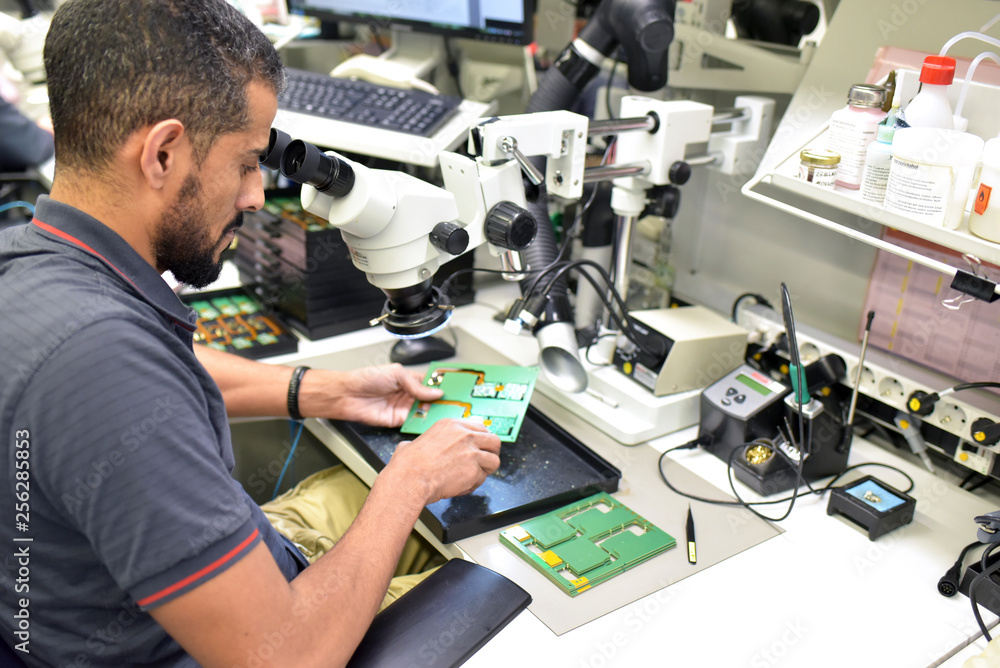 Man using a microscope for the quality control in the manufacturing of circuit boards for the electronics industry Man using a microscope for the quality control in the manufacturing of circuit boards for the electronics industry