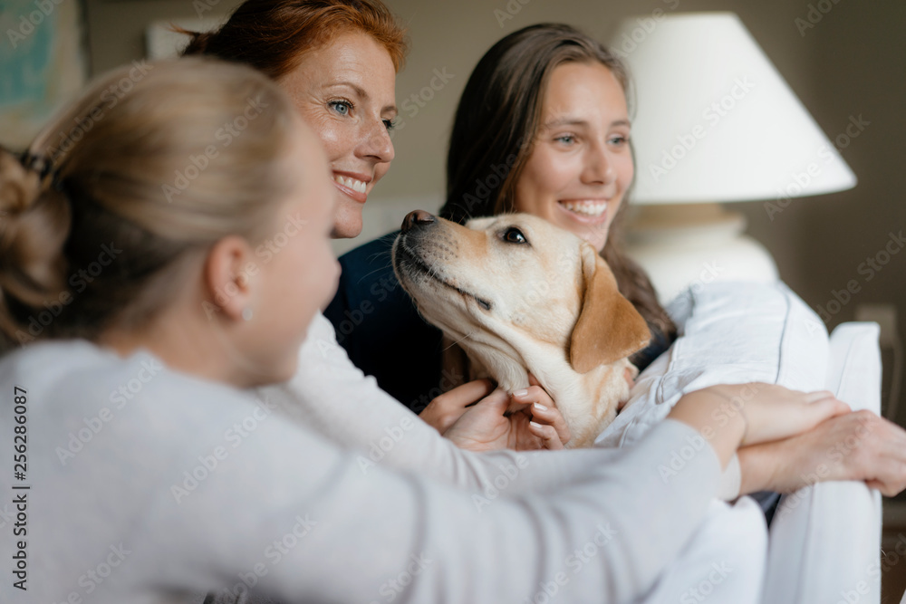 Happy mother with two teenage girls and dog on couch at home Happy mother with two teenage girls and dog on couch at home