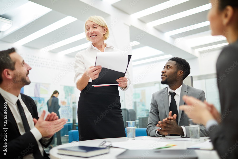 Multi-ethnic group of people sitting at table during meeting in office, focus on mature businesswoman giving presentation Multi-ethnic group of people sitting at table during meeting in office, focus on mature businesswoman giving presentation