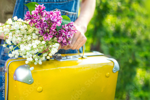 Fototapeta Naklejka Na Ścianę i Meble -  Close-up hand holding flowers and suitcase, spring travel concept