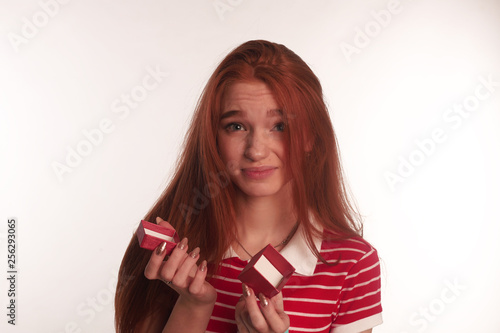The portrait of an young redhead lady with a gift box in her hands isolated over white background posing
