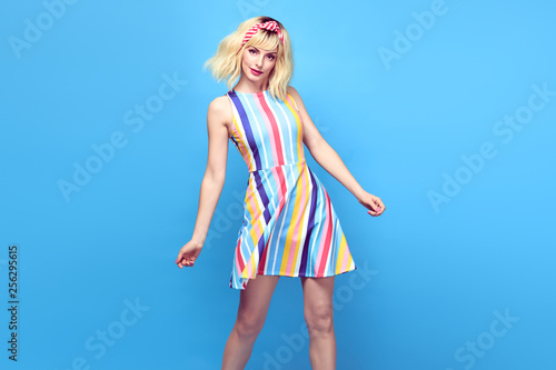 Fashionable shapely Young woman smiling on blue background. Excited blonde Girl Having Fun dance in Trendy summer dress, Stylish fashion sneakers, makeup. Happiness funny concept