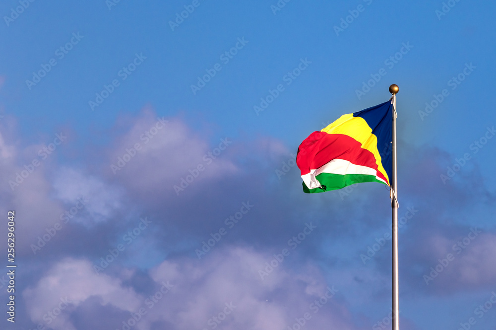 The flag of Seychelles over a blue sky with clouds