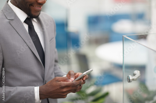 Cropped shot of smiling African businessman holding smartphone in hand, copy space photo