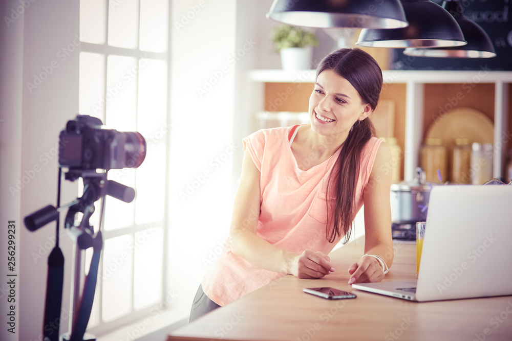 Young woman in kitchen with laptop computer looking recipes, smiling. Food blogger concept. Young woman in kitchen with laptop computer looking recipes, smiling. Food blogger concept.