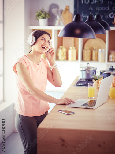 Young woman in kitchen with laptop computer looking recipes  smiling. Food blogger concept.