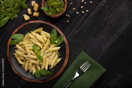 Penne pasta on black plate and black table with pesto sauce parmesan and basil. Italian food. Top view. Flat lay. Copyspace for your text.