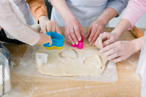 Two sisters, grandmother and little baby daughter are cooking in the kitchen to Mothers day, lifestyle photo series in bright home interior. Hands cutting hearts cookies from dough fom mother's day