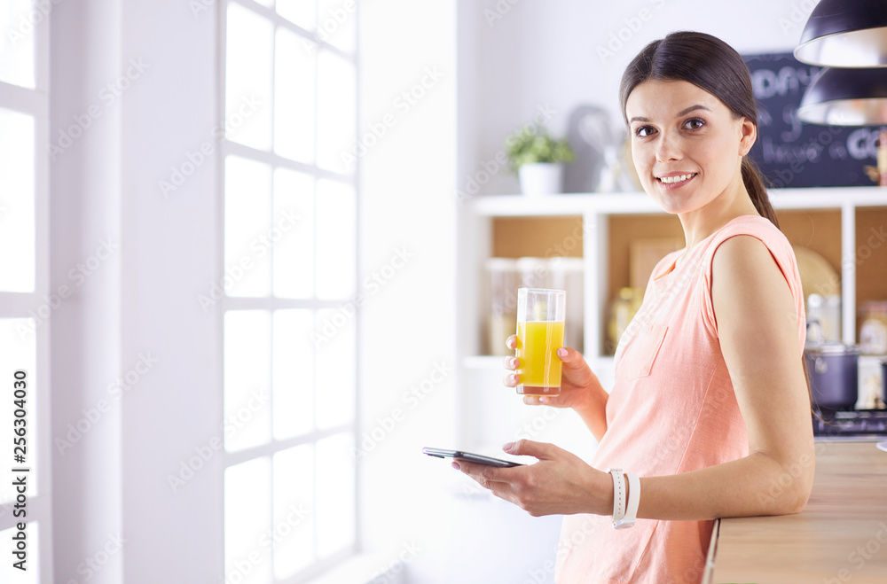 Smiling pretty woman looking at mobile phone and holding glass of orange juice while having breakfast in a kitchen. Smiling pretty woman looking at mobile phone and holding glass of orange juice while having breakfast in a kitchen.