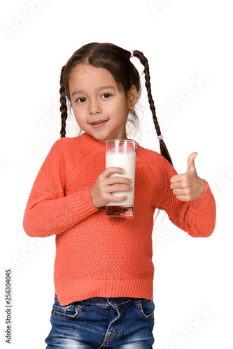 Portrait of cute little child girl holding glass of milk and showing thumb up isolated on white