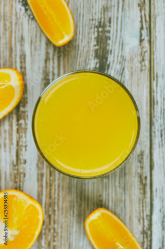 A glass of fresh orange juice and orange fruits on a wooden table. vertical view close-up. refreshing citrus drink.