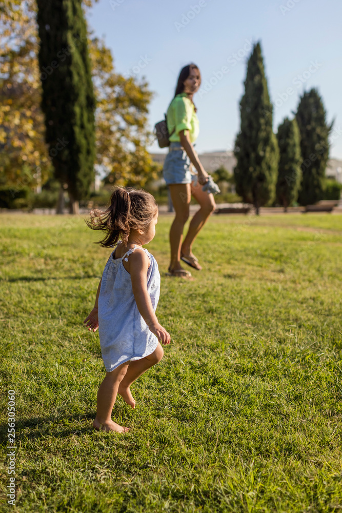 Little girl walking on lawn in a park with her mother Little girl walking on lawn in a park with her mother
