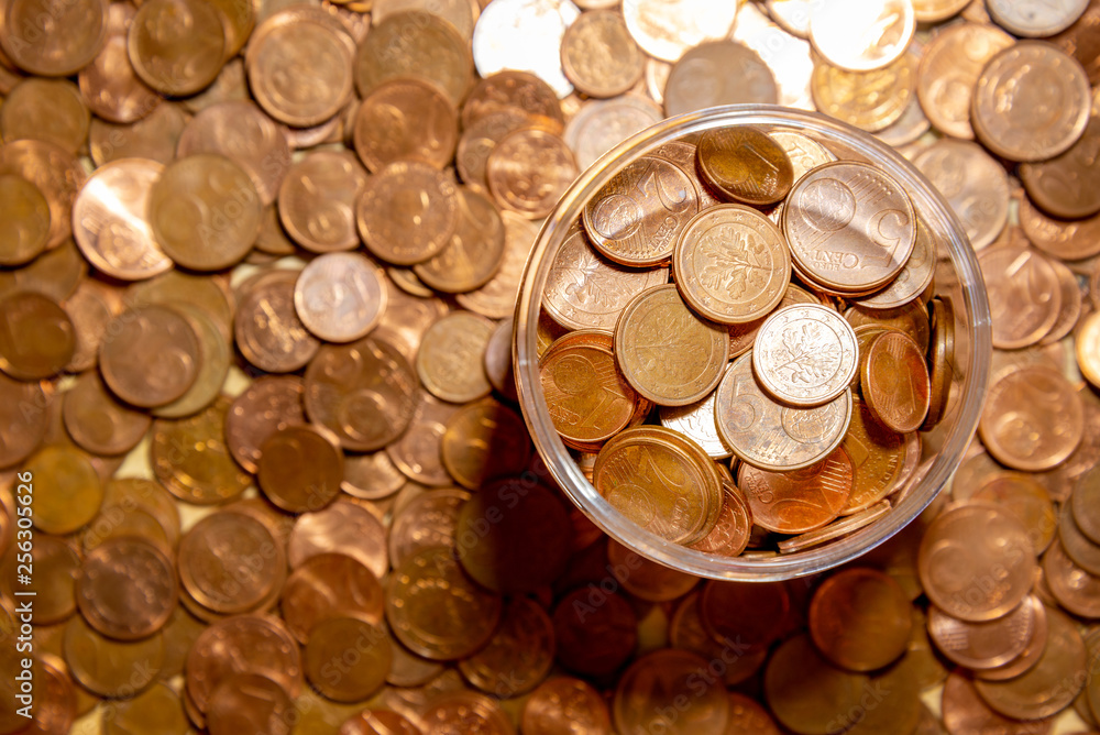 Copper cent, one, two and five euro coins in open circle glass bottle on cent coins background, selected focus. Saving and collect money. Copper cent, one, two and five euro coins in open circle glass bottle on cent coins background, selected focus. Saving and collect money.